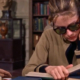 Image of Audrey Hepburn in the library reading a book and wearing sunglasses.