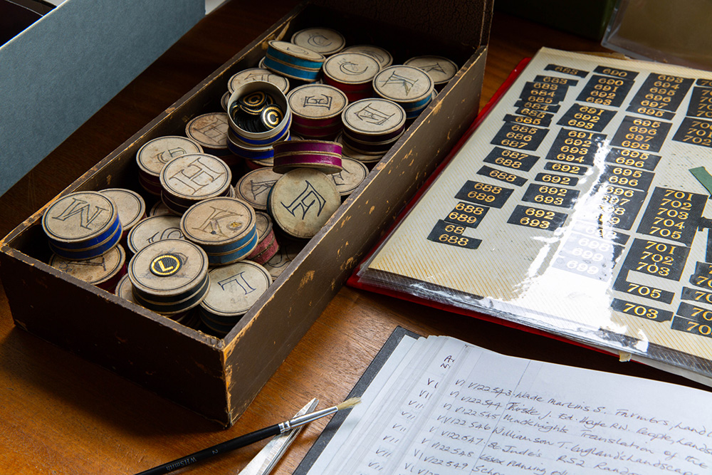 Wooden box of vintage tokens beside a numbered score chart and handwritten notes on a table