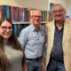 Gibson Library Society Secretary, Chairman and Treasurer standing together in front of bookshelves filled with fiction novels.