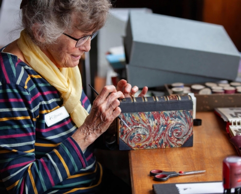 Image of a woman in glasses carefully painting a book spine