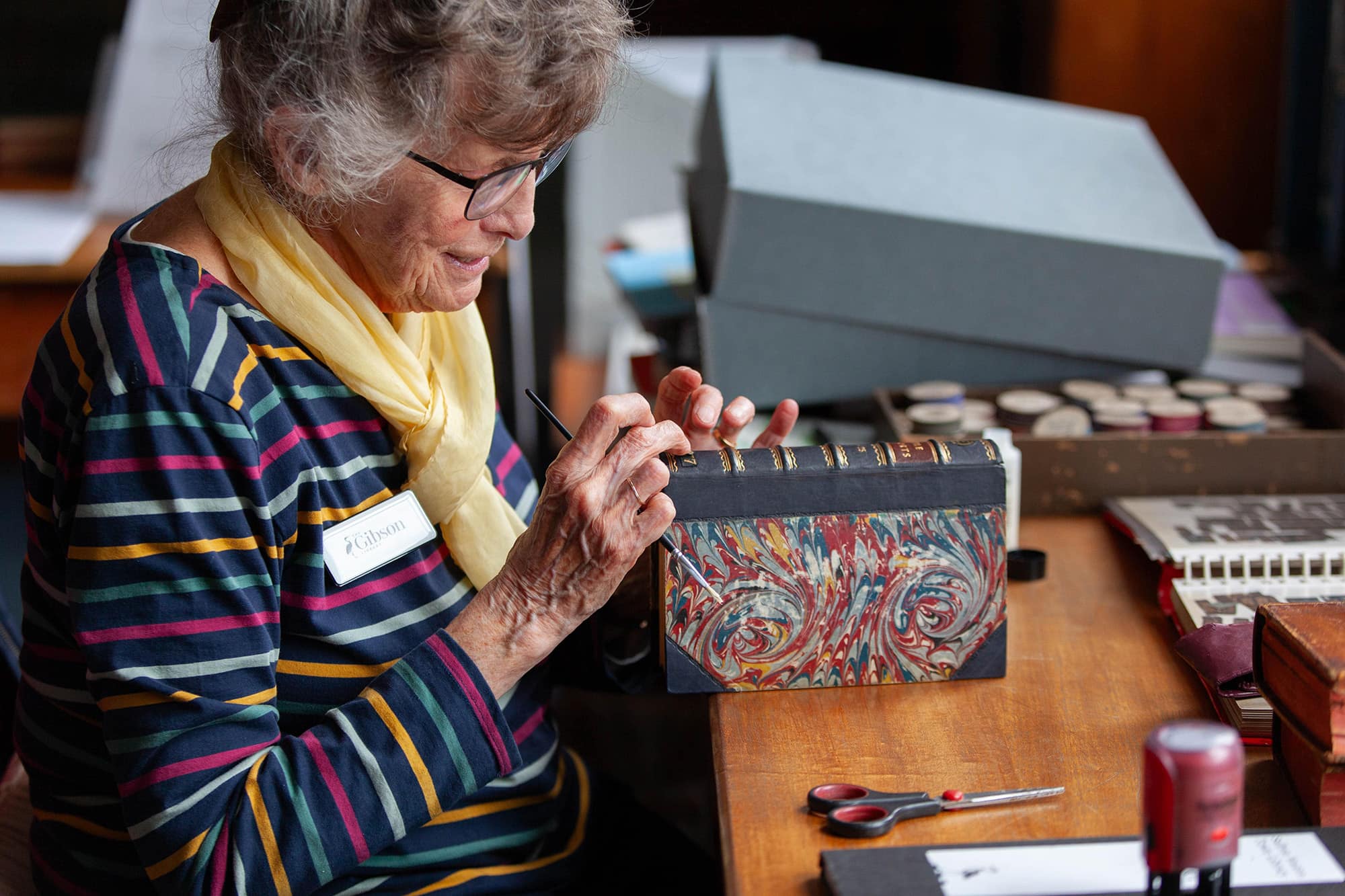 Image of a woman in glasses carefully painting a book spine