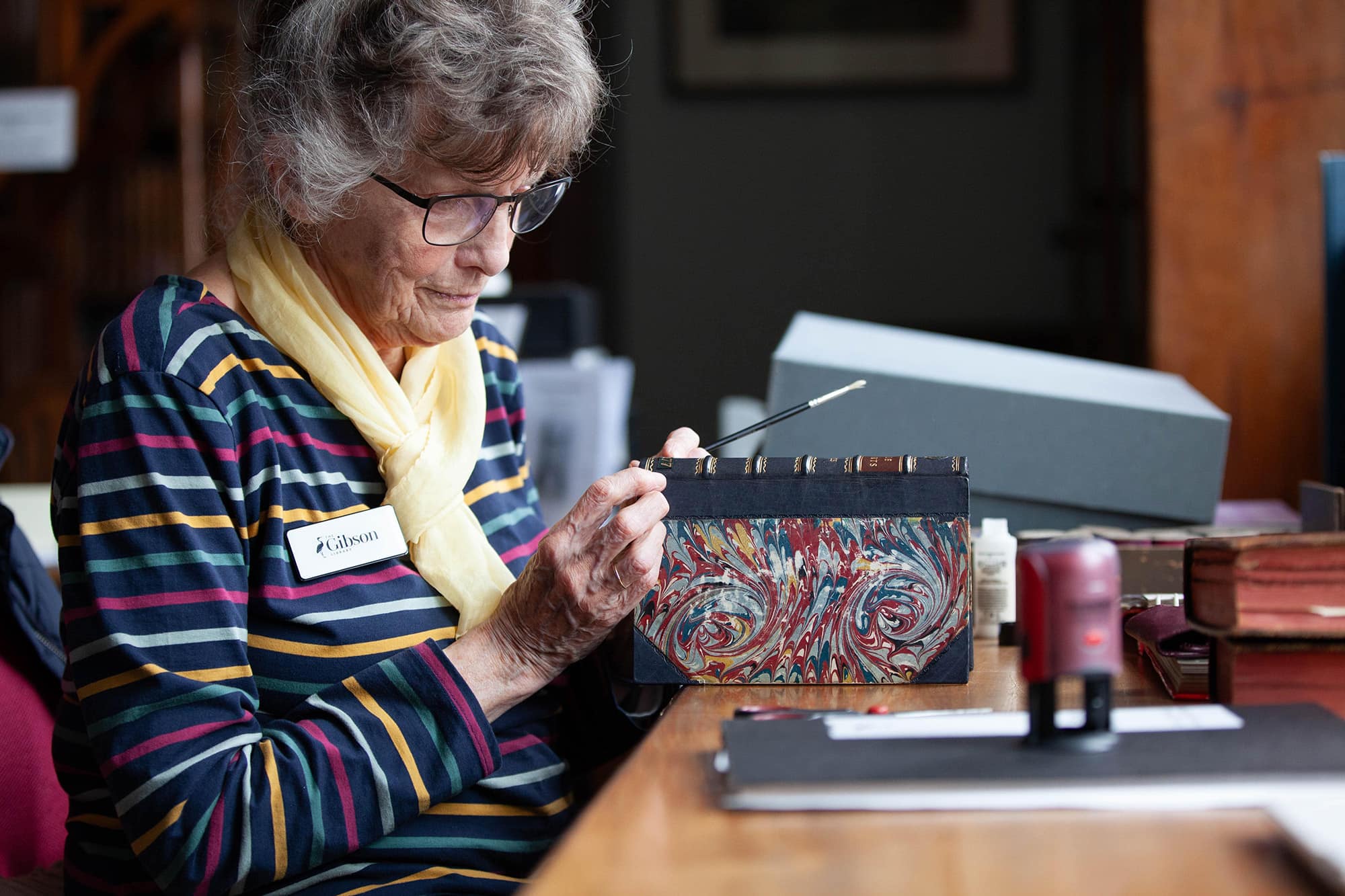 Image of a woman in glasses carefully painting a book