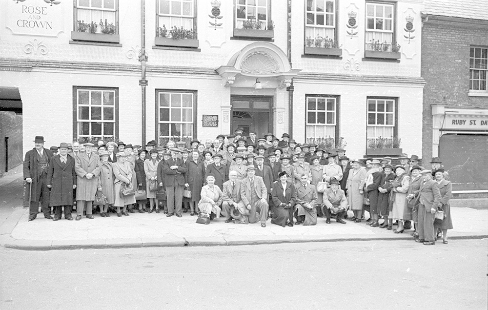 A vintage black and white photograph of a large group of people gathered on the pavement outside the historic Rose and Crown Hotel in Saffron Walden.