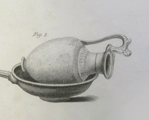 An antique engraving labeled Fig. 1 showing an ornate decorative ewer resting on its side inside a shallow, handled pan.