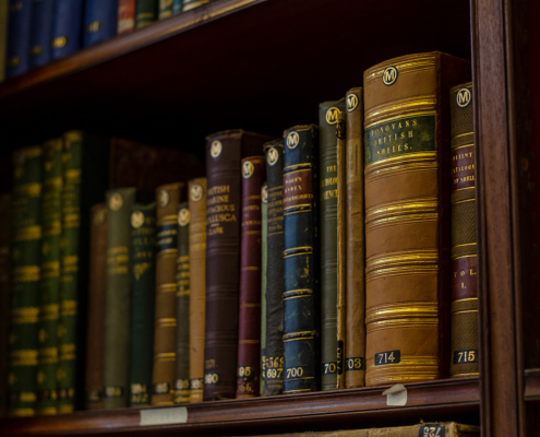 A row of old, leather-bound antique books on a library shelf, prominently featuring the gold-lettered spine of "Donovan's British Shells"